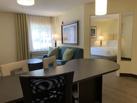 Una habitación de hotel con una mesa de comedor, un sofá, una cama y una ventana con cortinas.