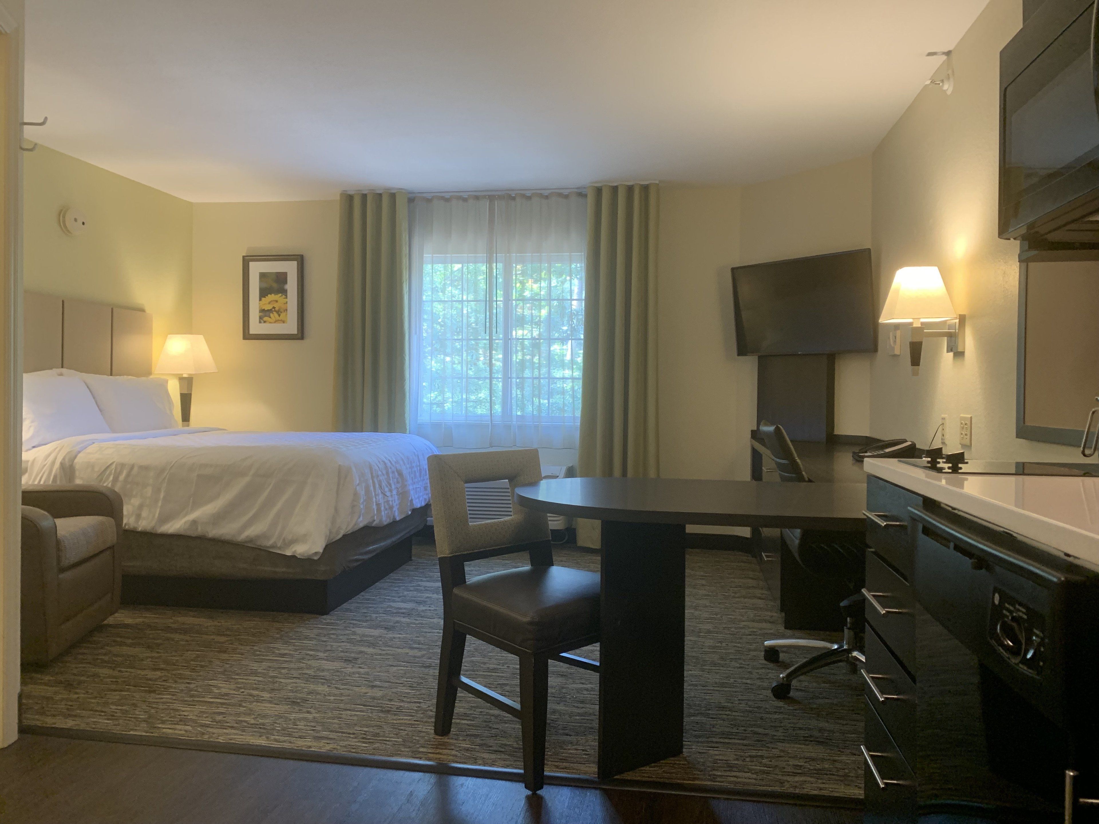 A hotel room with a bed, a desk, a chair, a TV, and a bathroom.