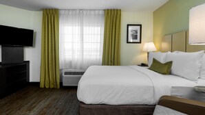 Una habitación de hotel con una cama, televisión, lámpara y ventana con cortinas.