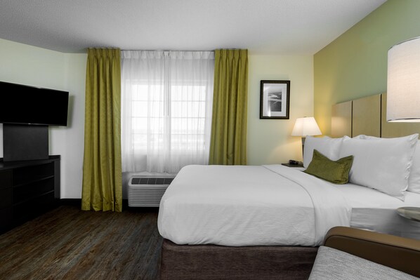 Een hotelkamer met een bed, een televisie, een lamp en een raam met gordijnen.