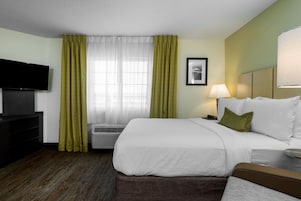 Una habitación de hotel con una cama, televisión, lámpara y ventana con cortinas.