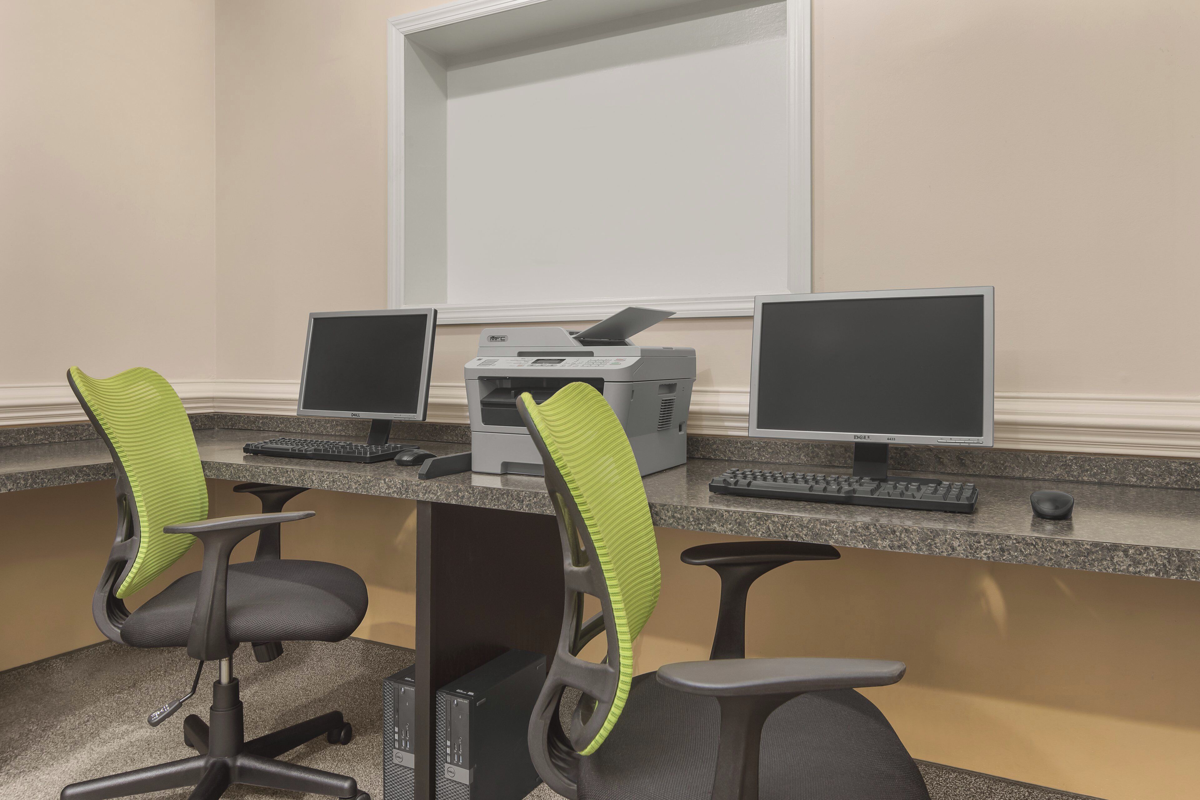 A workspace with two monitors, a printer, and two chairs with green backrests.