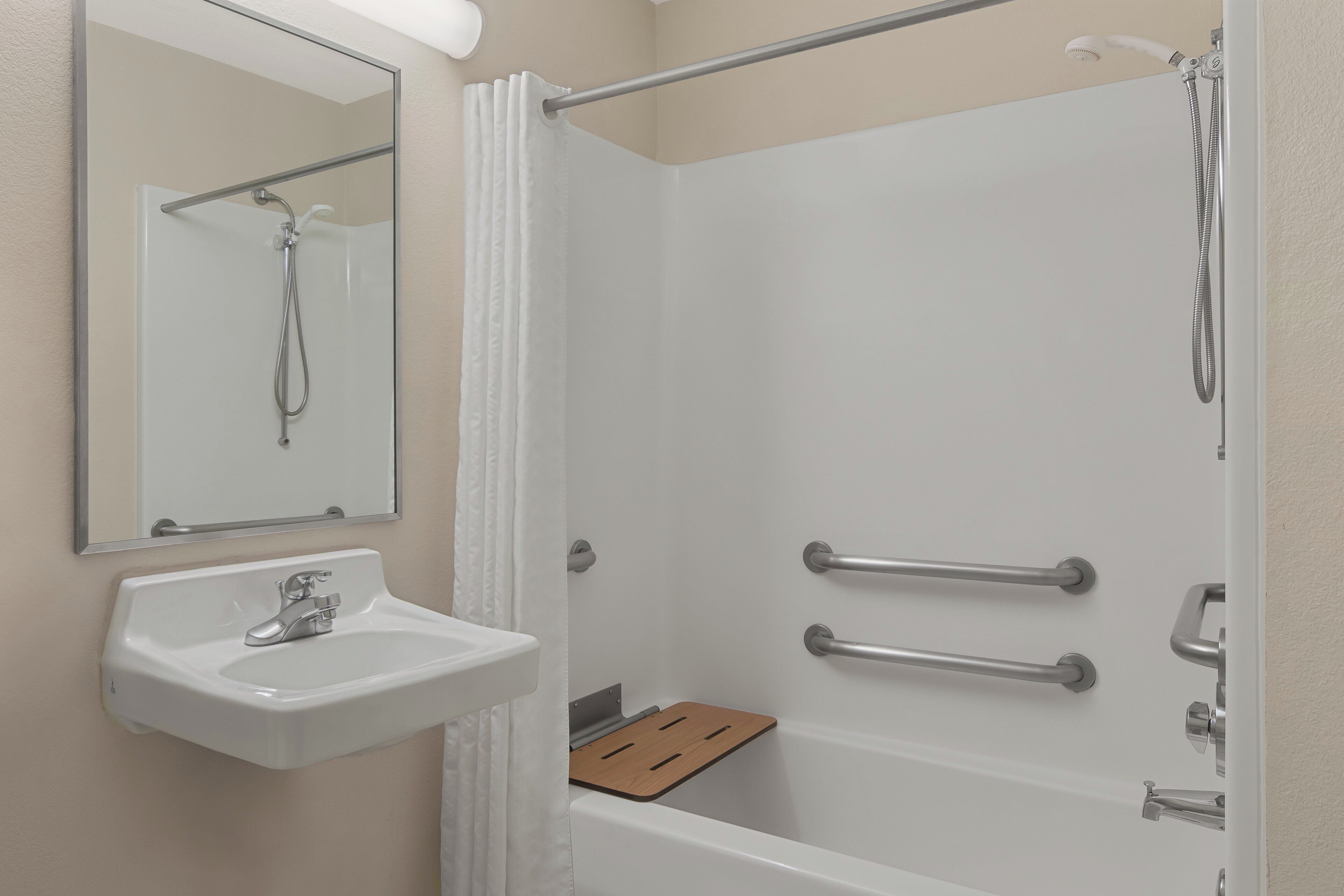A modern bathroom with a white sink, a mirror, a shower with a glass door, and a wooden shelf.