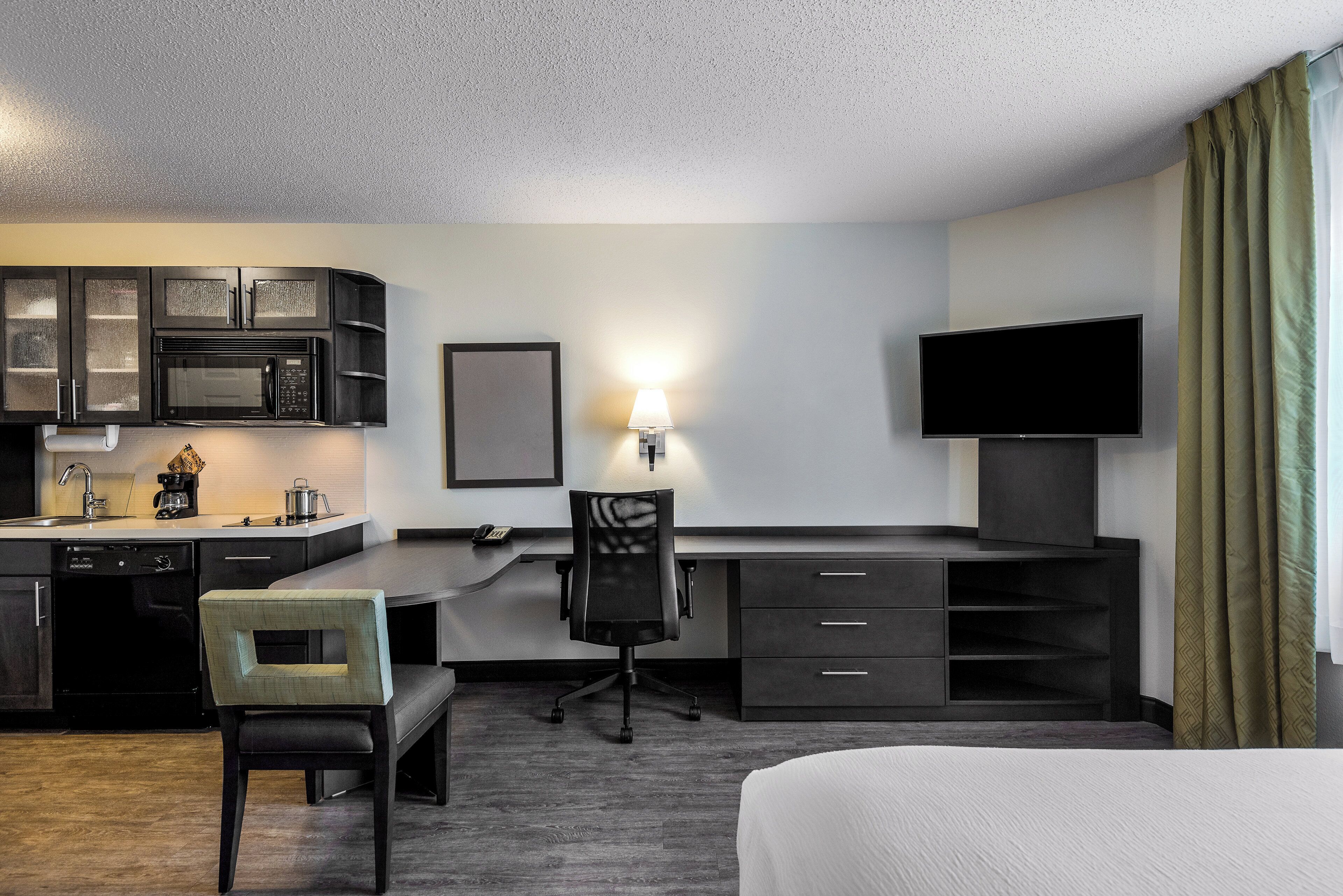 Habitación de hotel con kitchenette, escritorio con silla, televisión y cama.