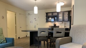 Una cocina moderna con armarios oscuros, microondas y cafetera. Hay un comedor con una mesa redonda y cuatro sillas.