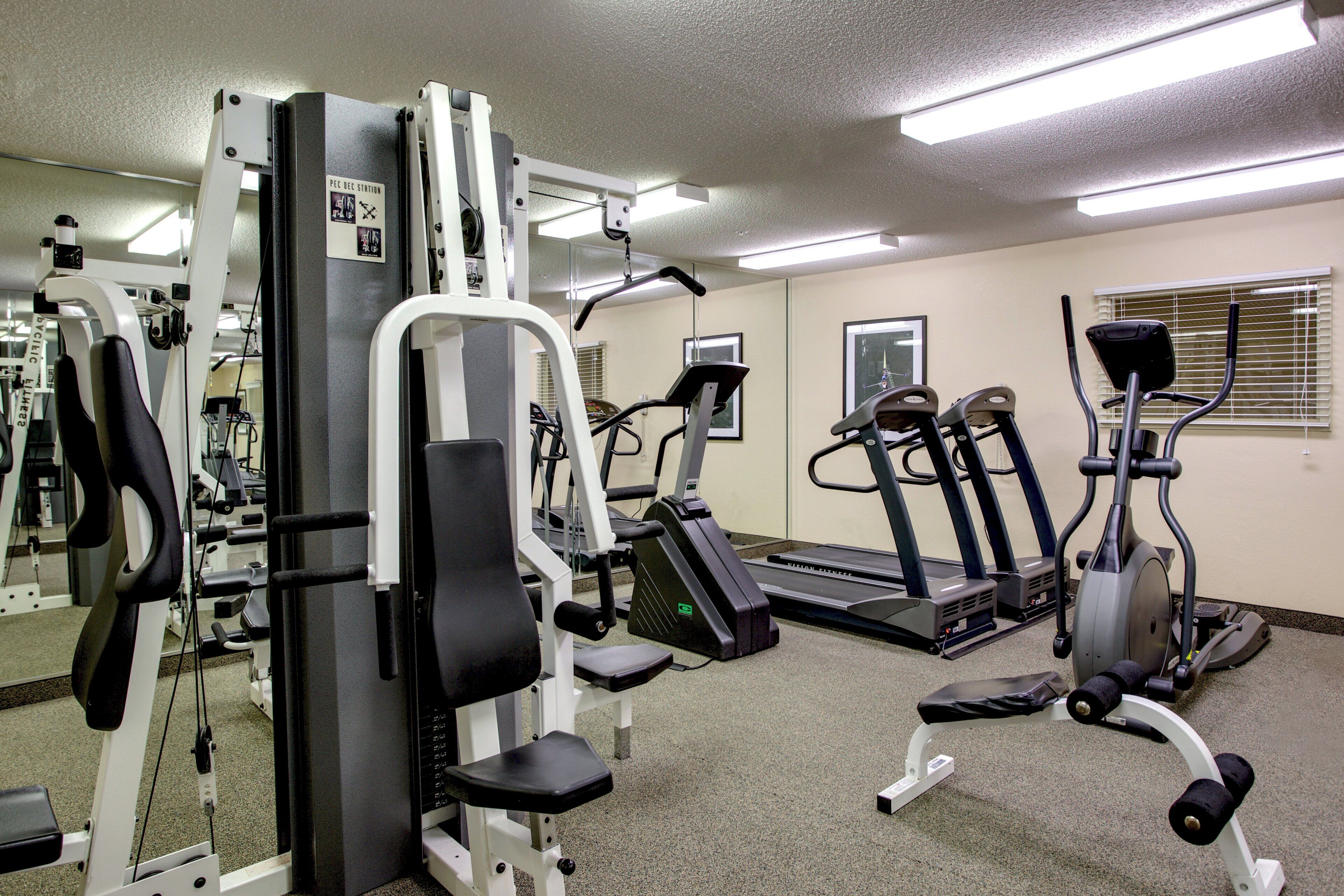 Une salle de sport équipée de divers appareils d’exercice, notamment une machine de musculation, des tapis de course et des appareils de type elliptique.
