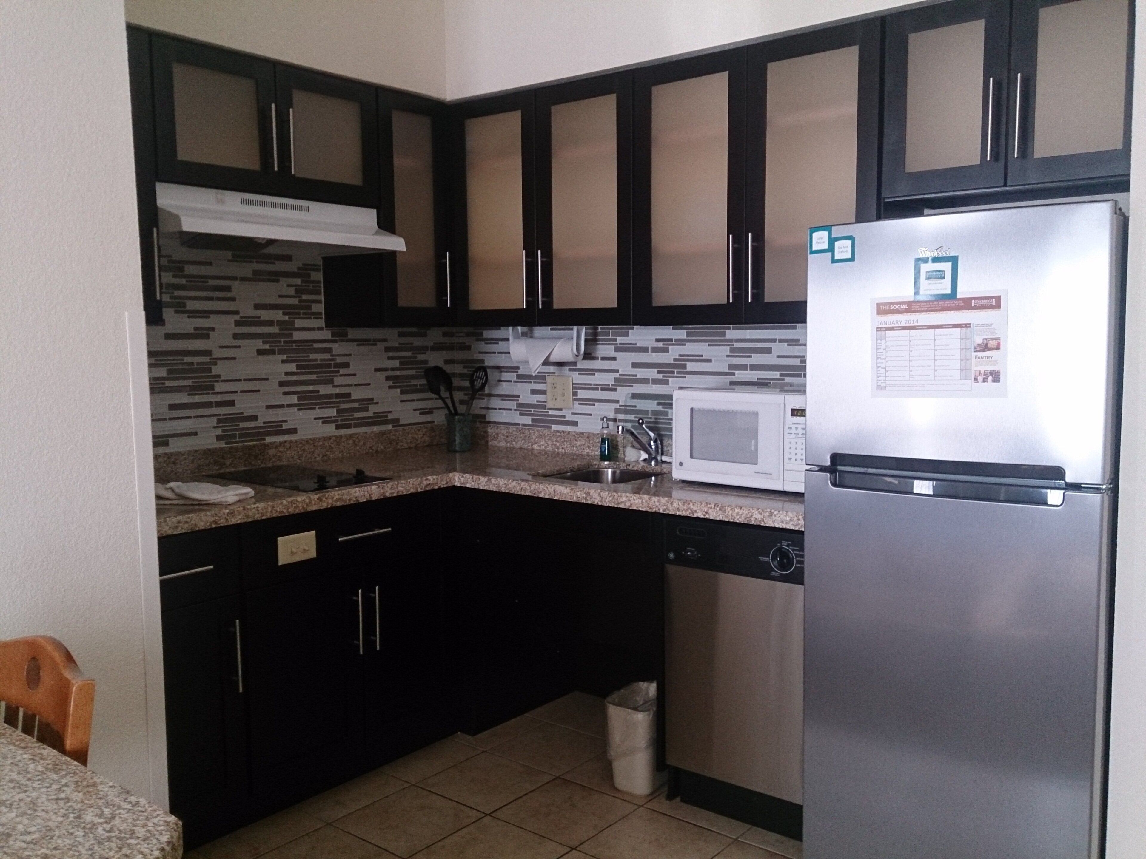 A kitchen with dark cabinets, a stainless steel refrigerator, a microwave, and a tiled backsplash.