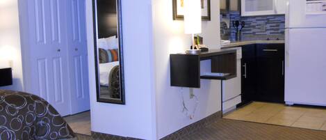 A hotel room with a bed, a bedside table, a mirror, a small kitchenette with a microwave, and a refrigerator.