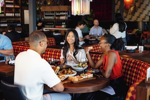 A group of people dining at a restaurant with booths and a bar in the background. - Staybridge Suites Charlotte Ballantyne by IHG (Charlotte)
