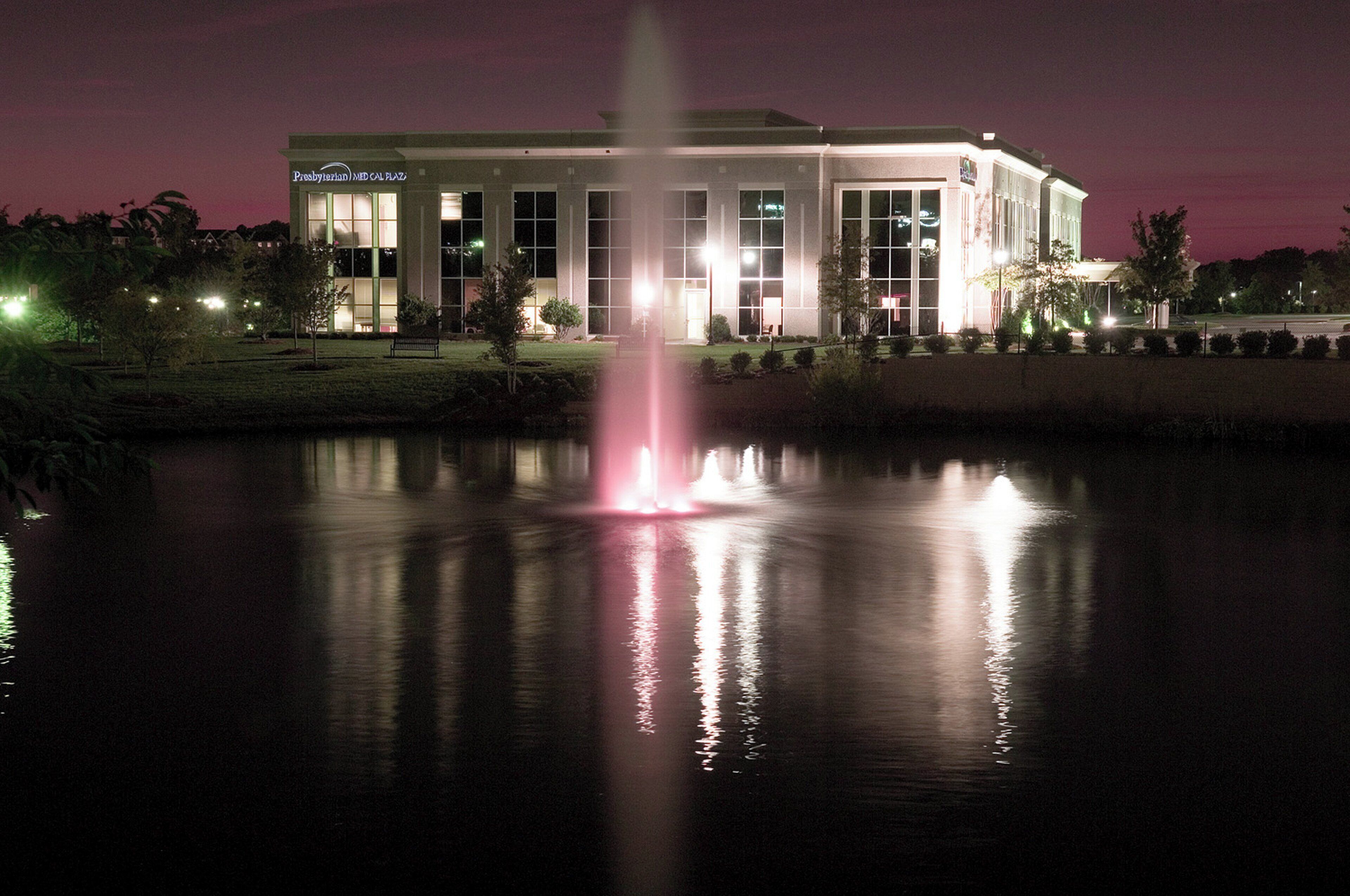 A building with a large water fountain in front, surrounded by a well-lit lawn and trees.