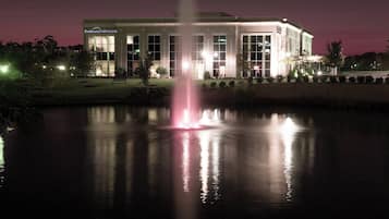 A building with a large water fountain in front, surrounded by a well-lit lawn and trees.
