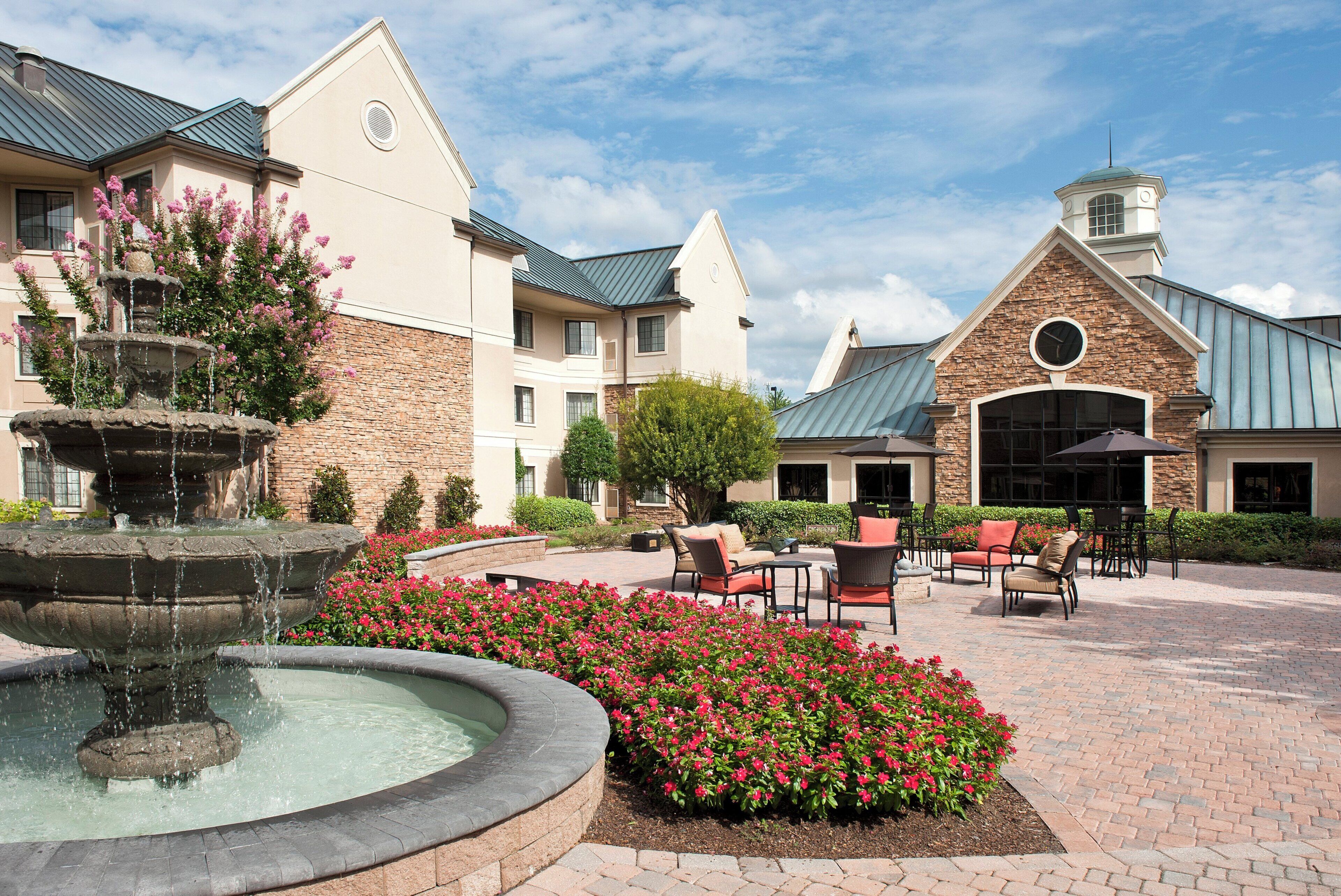 A courtyard with a fountain, outdoor seating, and a building with a stone facade and a clock tower.