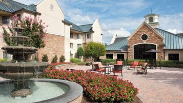 A courtyard with a fountain, outdoor seating, and a building with a stone facade and a clock tower.