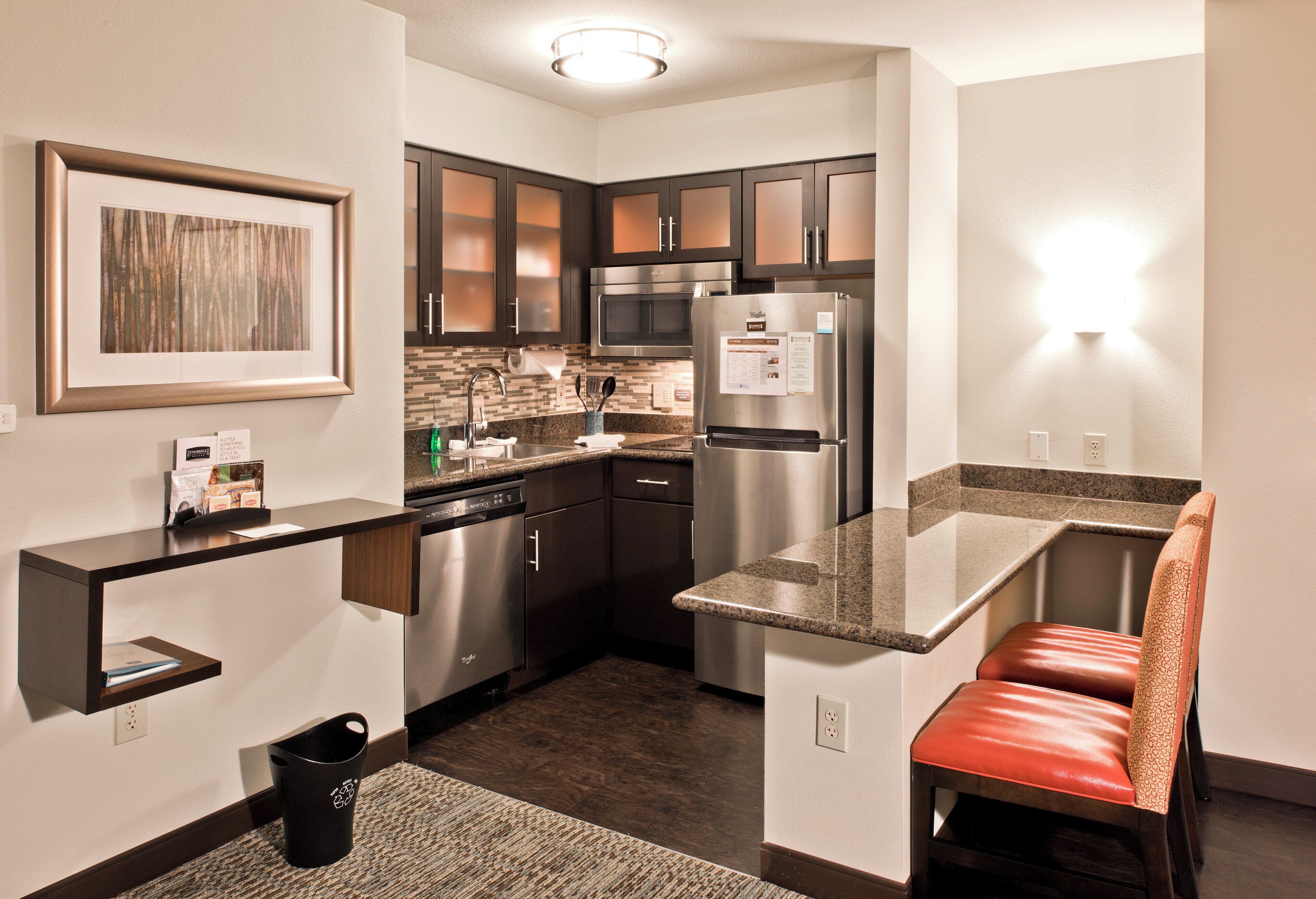 A compact kitchen with dark cabinets, a stainless steel refrigerator, a microwave, and a small seating area with a red bench.