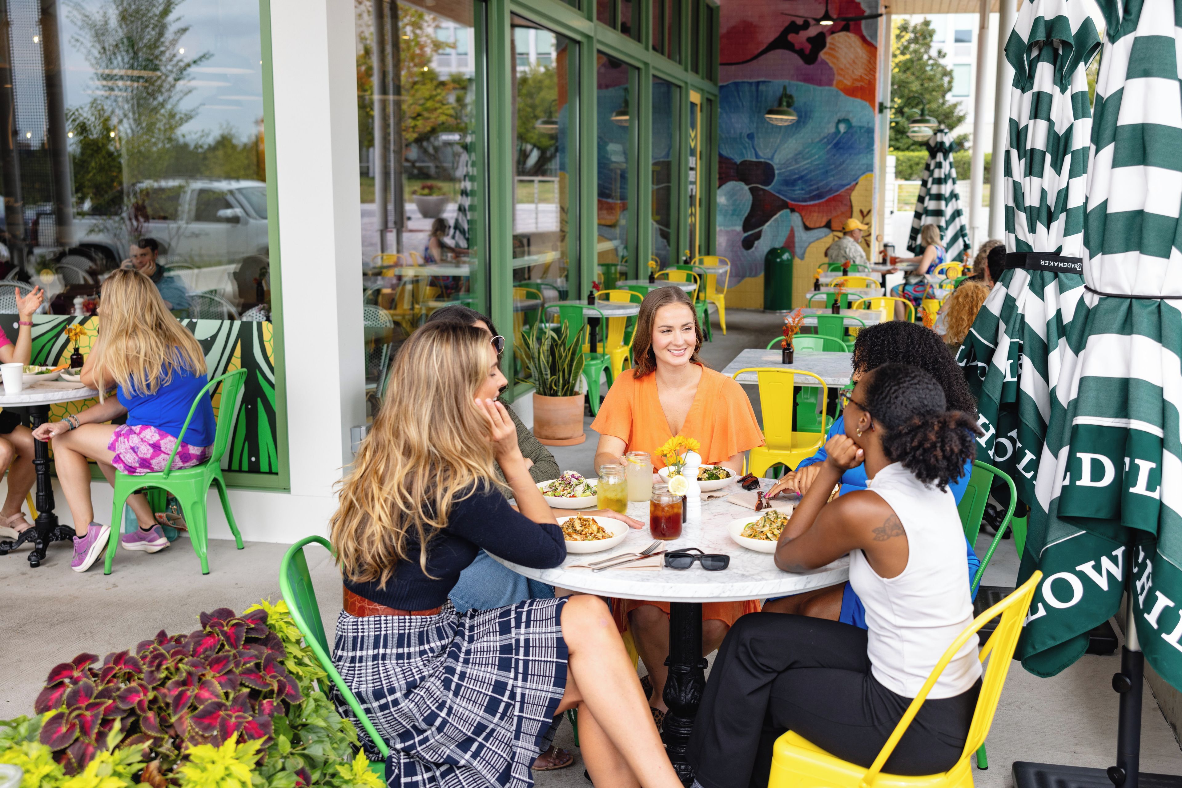 An outdoor dining area with tables and chairs, a mural on the wall, and a view of the street.