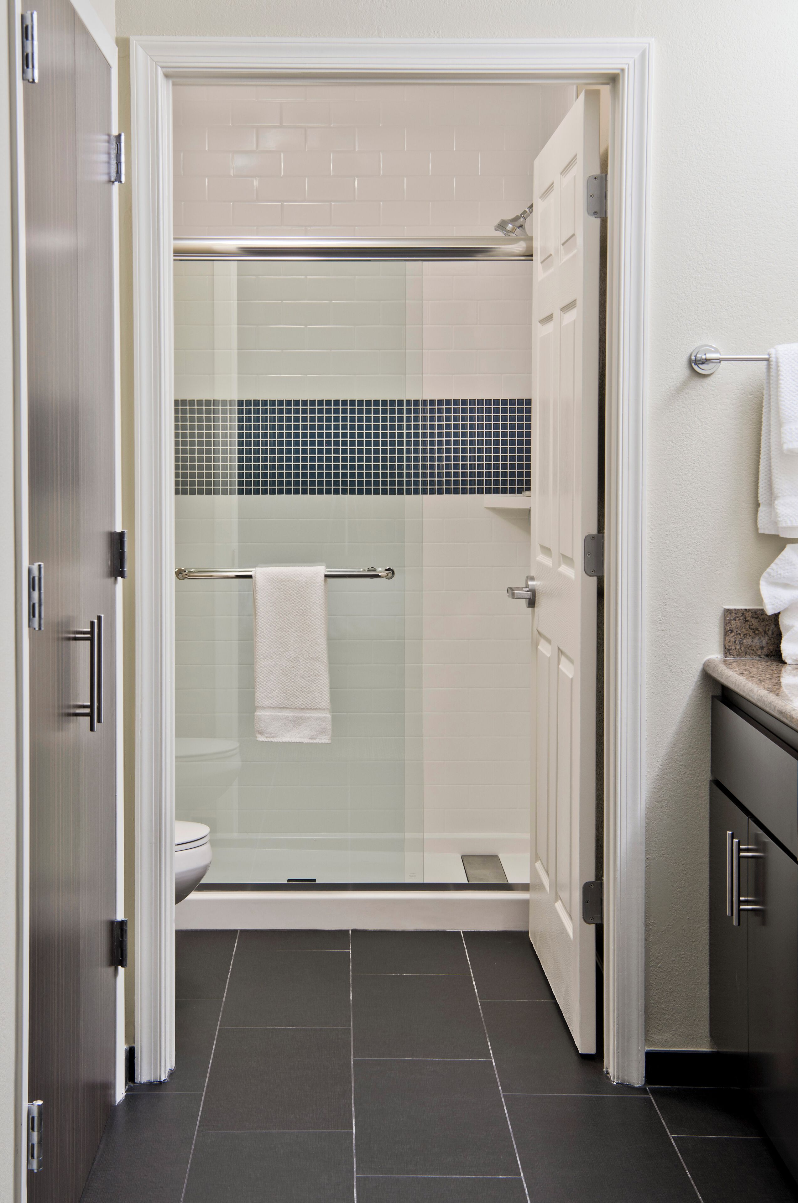 A modern bathroom with a glass-enclosed shower, white tiled walls, and a dark floor.
