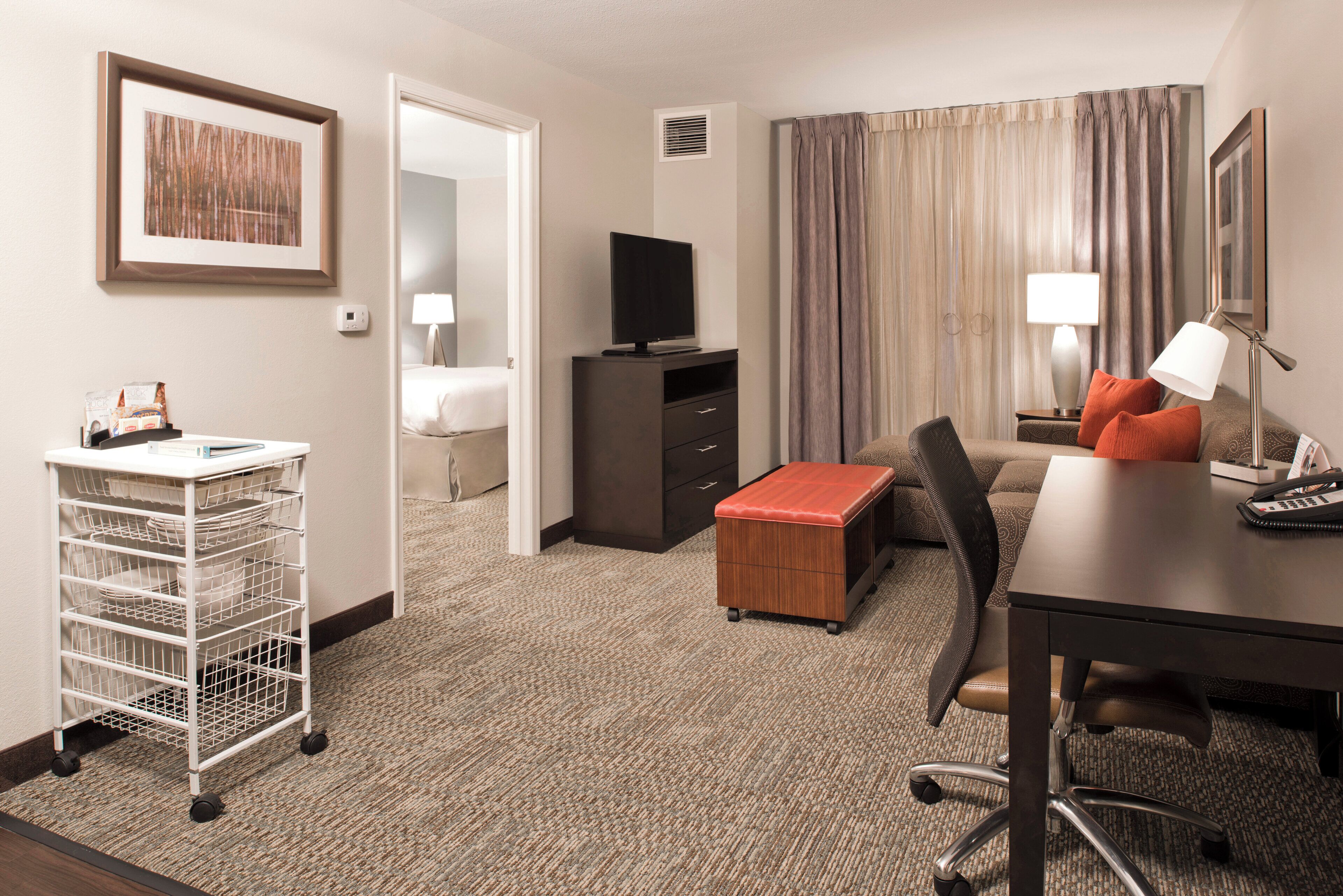 Una habitación de hotel con cama, escritorio, silla, televisor, lámpara, teléfono y una mesita.