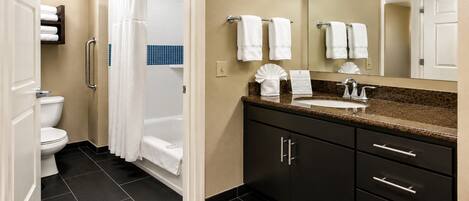 Un baño de hotel con inodoro, ducha, lavabo y armarios de tonos oscuros.