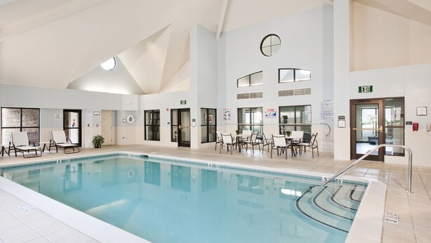 Una piscina interior con agua cristalina, rodeada de sillones y mesas, y con señal de salida.