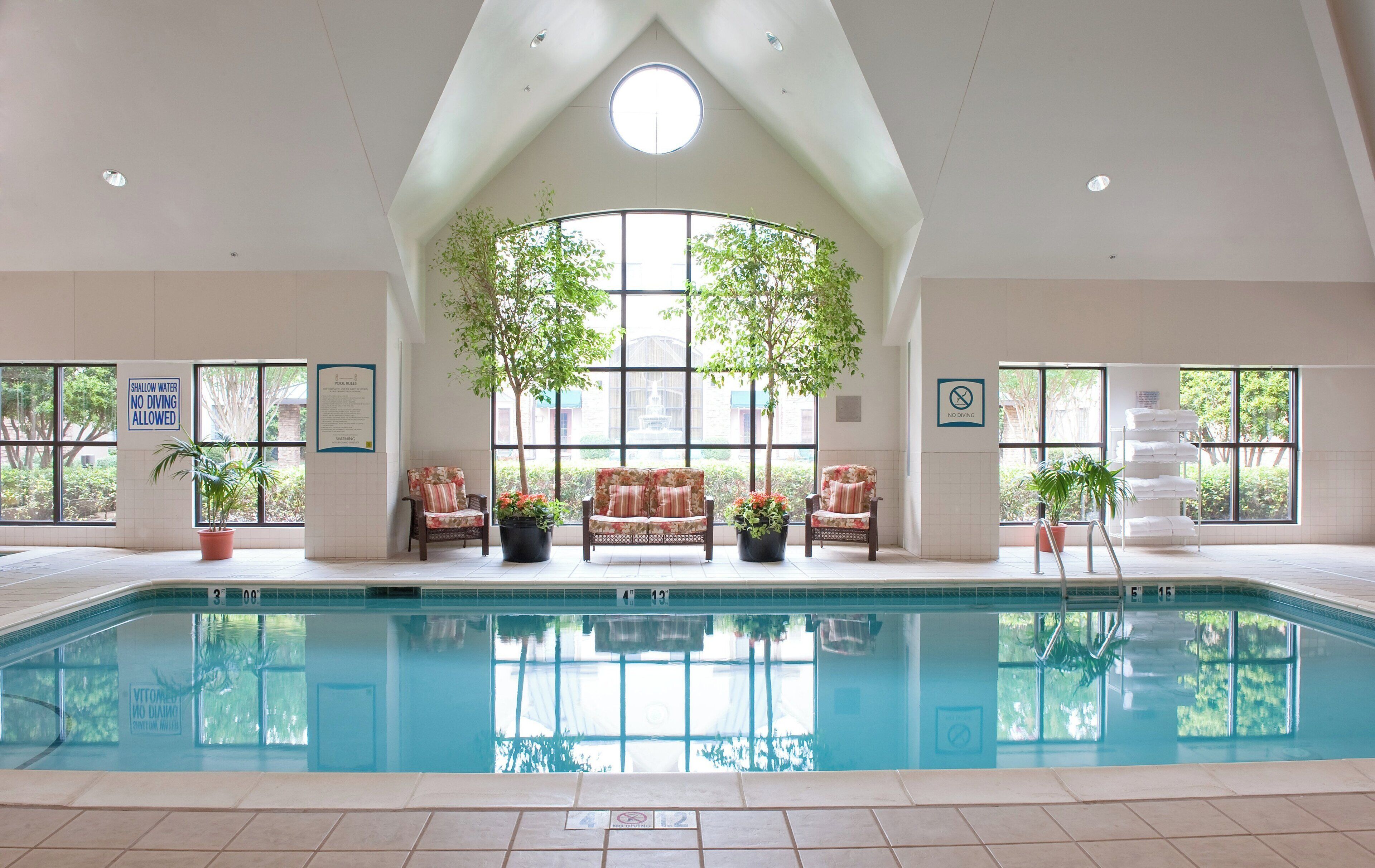 En indendørs swimmingpool med højt til loftet, store vinduer og siddeområder med plantekasser.