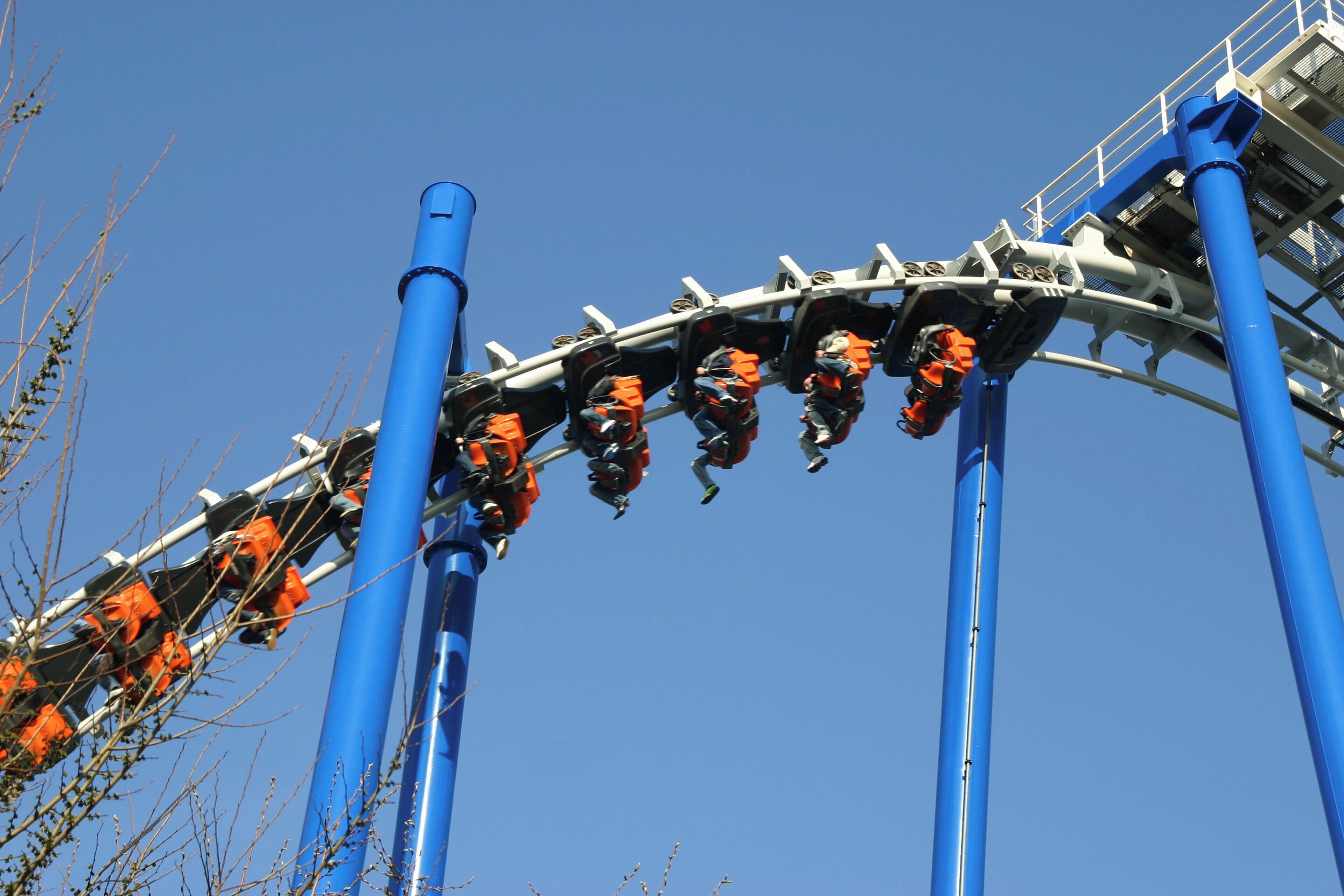 A roller coaster with riders in harnesses, blue support structures, and a clear sky.