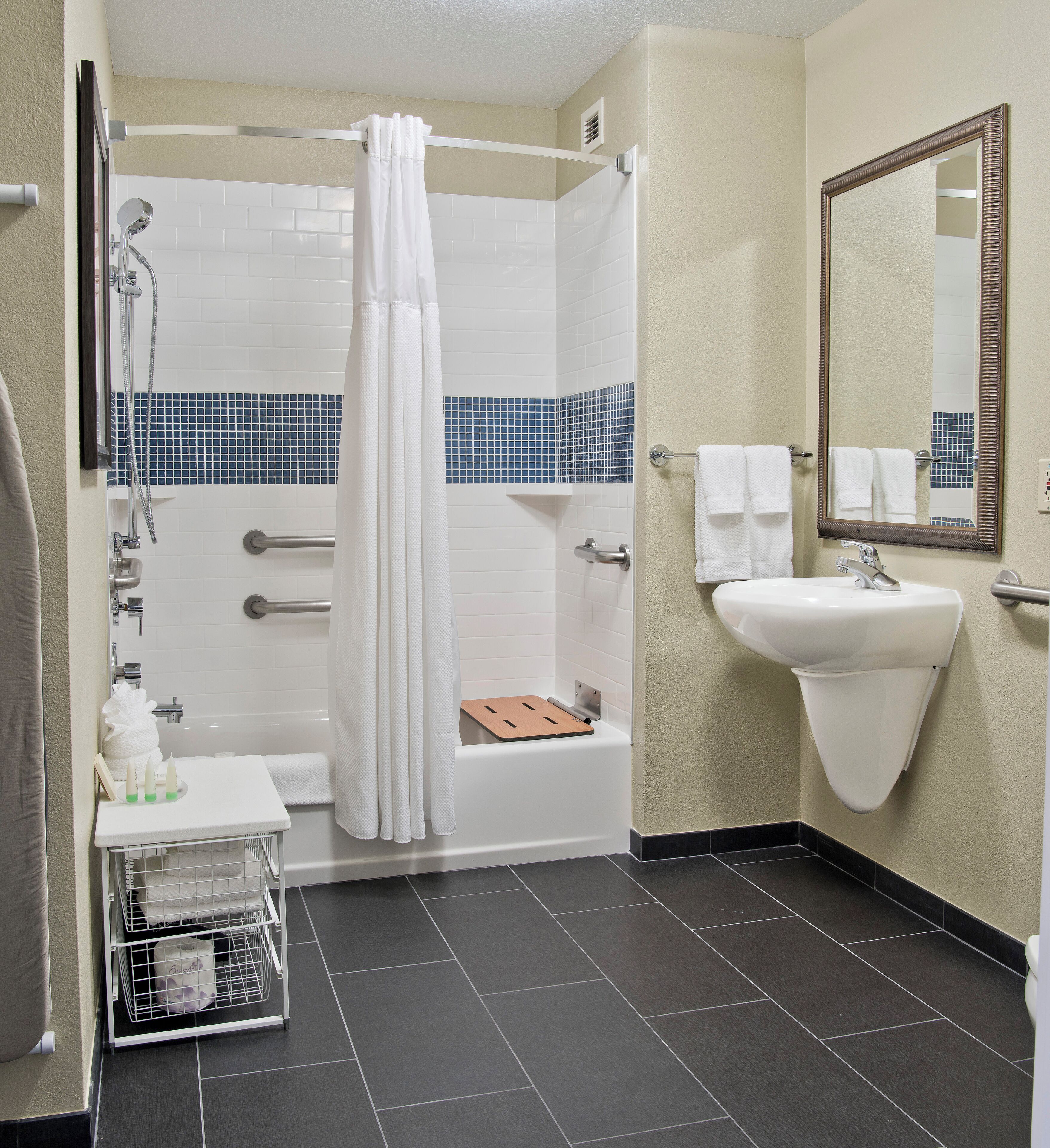 A bathroom with a shower, a sink, a mirror, and a towel rack.