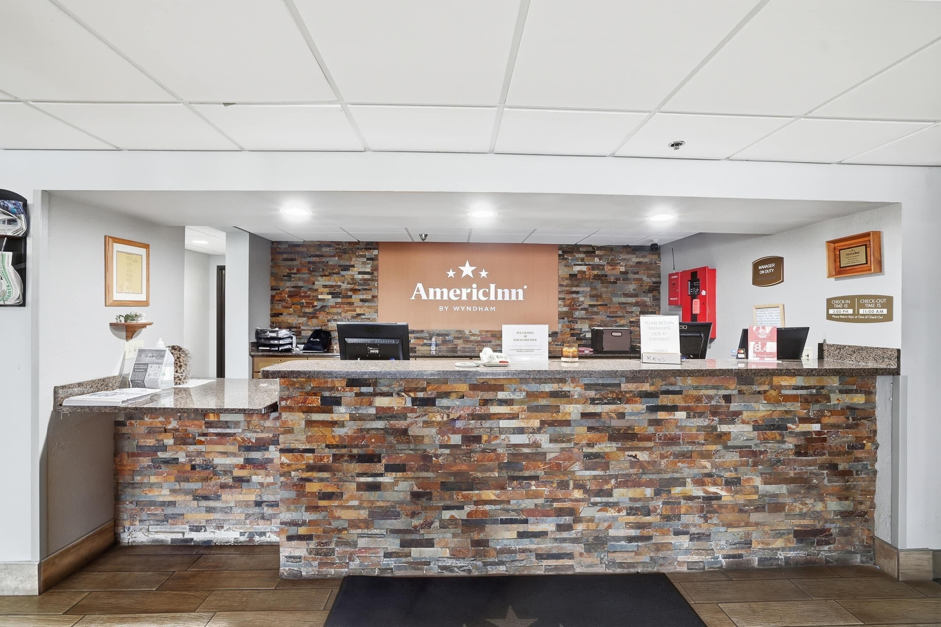 A reception desk with a stone facade, a sign reading 'AmericInn by Wyndham,' and a digital kiosk.