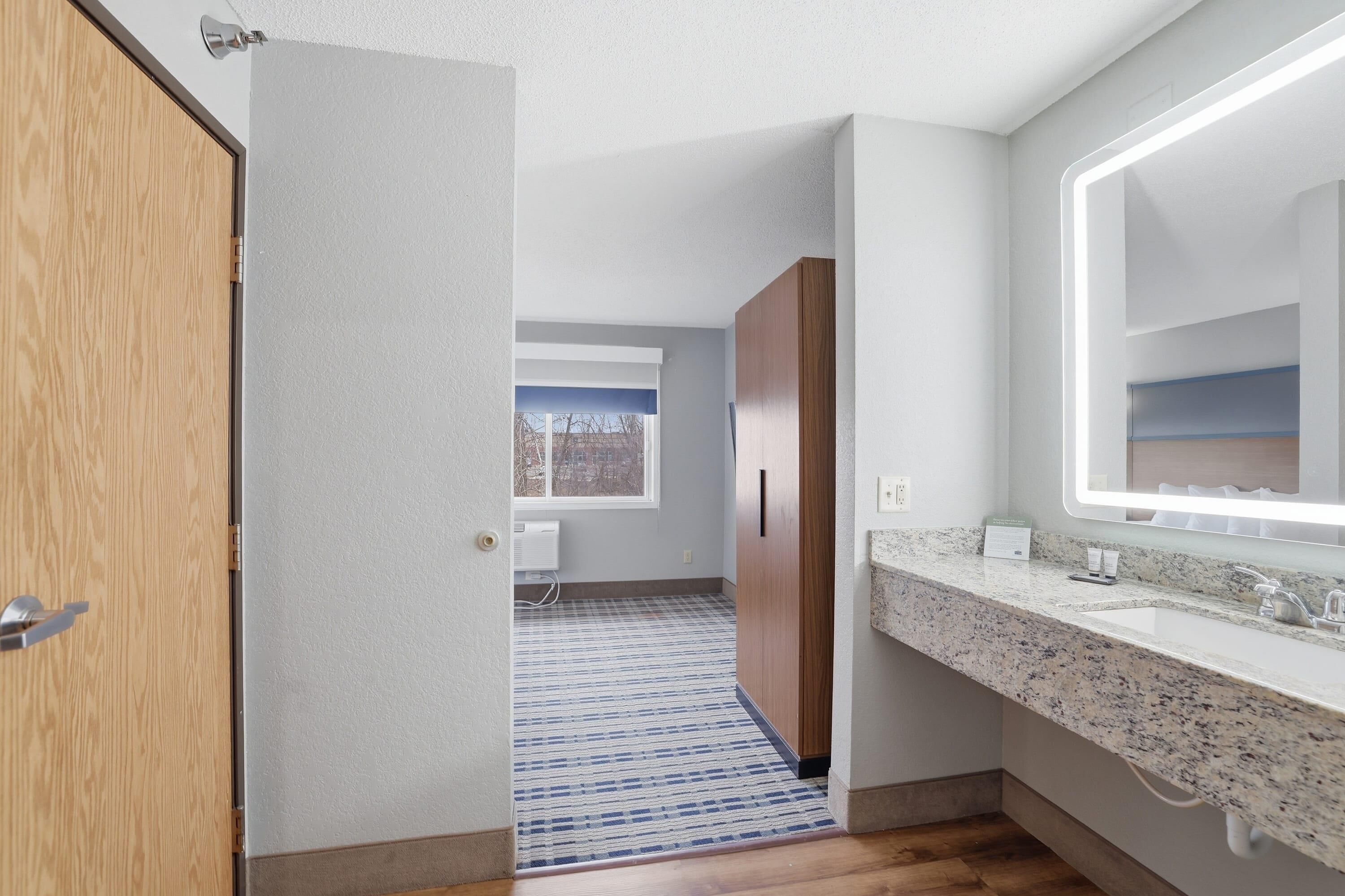 Une salle de bain moderne avec un comptoir en granit, un grand miroir et une armoire en bois.
