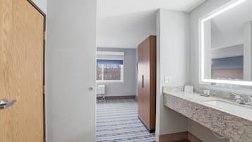 Une salle de bain moderne avec un comptoir en granit, un grand miroir et une armoire en bois.