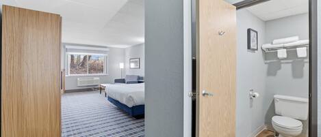 A hotel room with a bed, a bathroom, and a view of the outdoors.