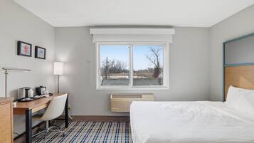 Una camera d'hotel con un letto, una scrivania, una sedia e una finestra che dà su un parcheggio.