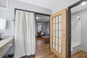 A bathroom with a shower, a wooden door, a sink, and a mirror. - AmericInn by Wyndham White Bear Lake St. Paul (White Bear Lake)
