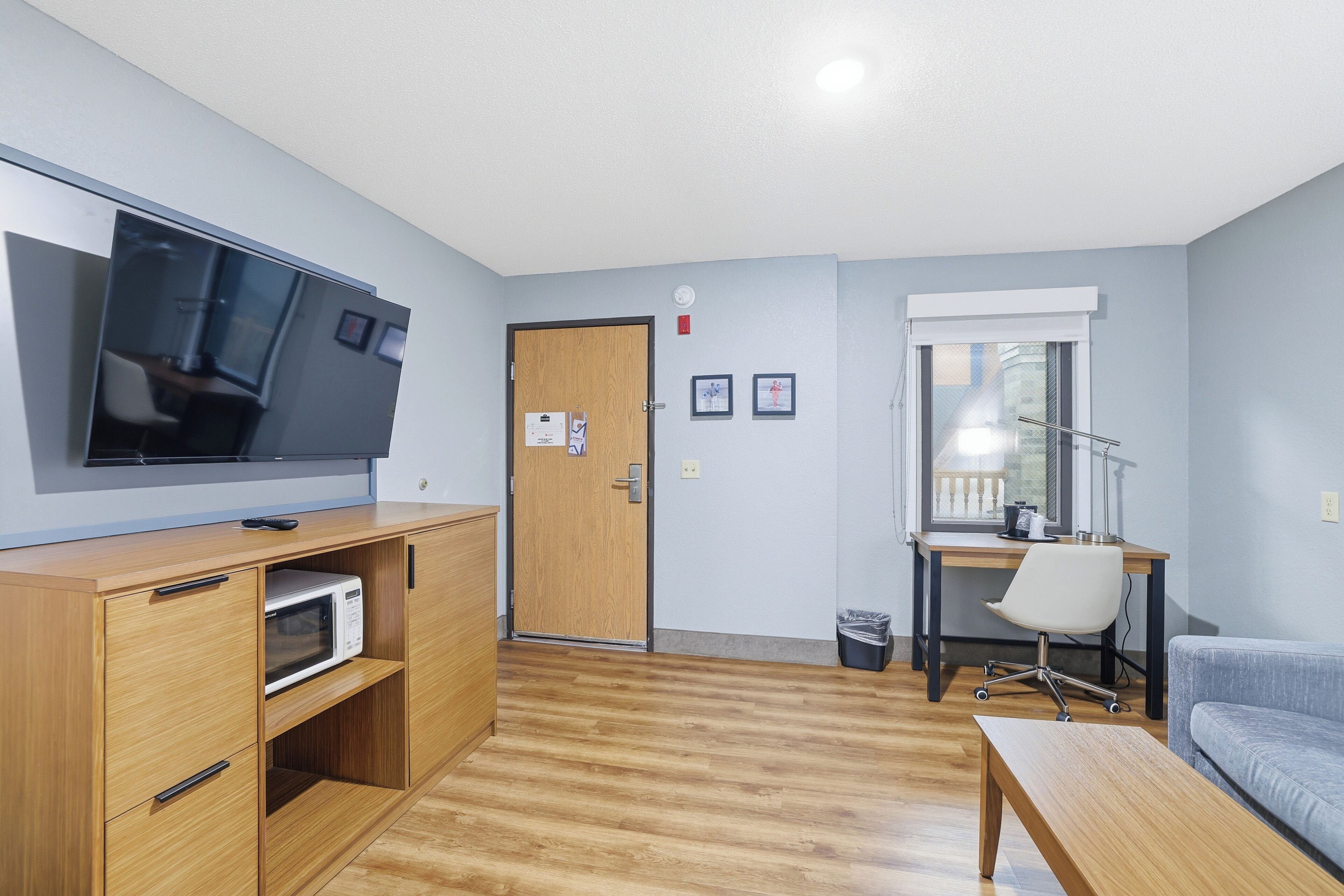 A compact living space with a wooden cabinet, a flat-screen TV, a desk with a chair, and a sofa.