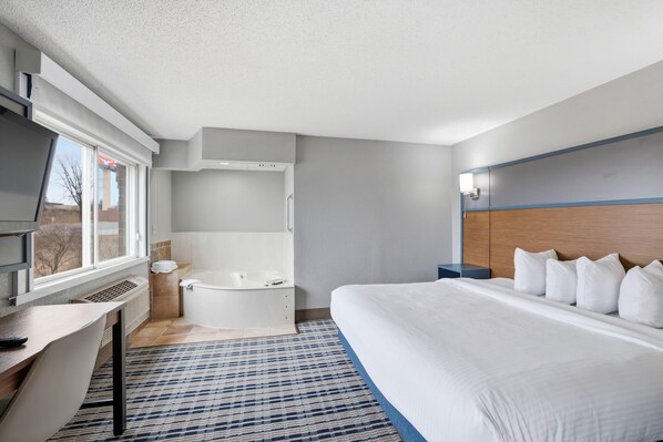 A hotel room with a bed, a desk, a window, a bathtub, and a headboard.
