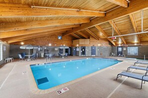 An indoor swimming pool with a wooden ceiling, lounge chairs, and a tiled floor.