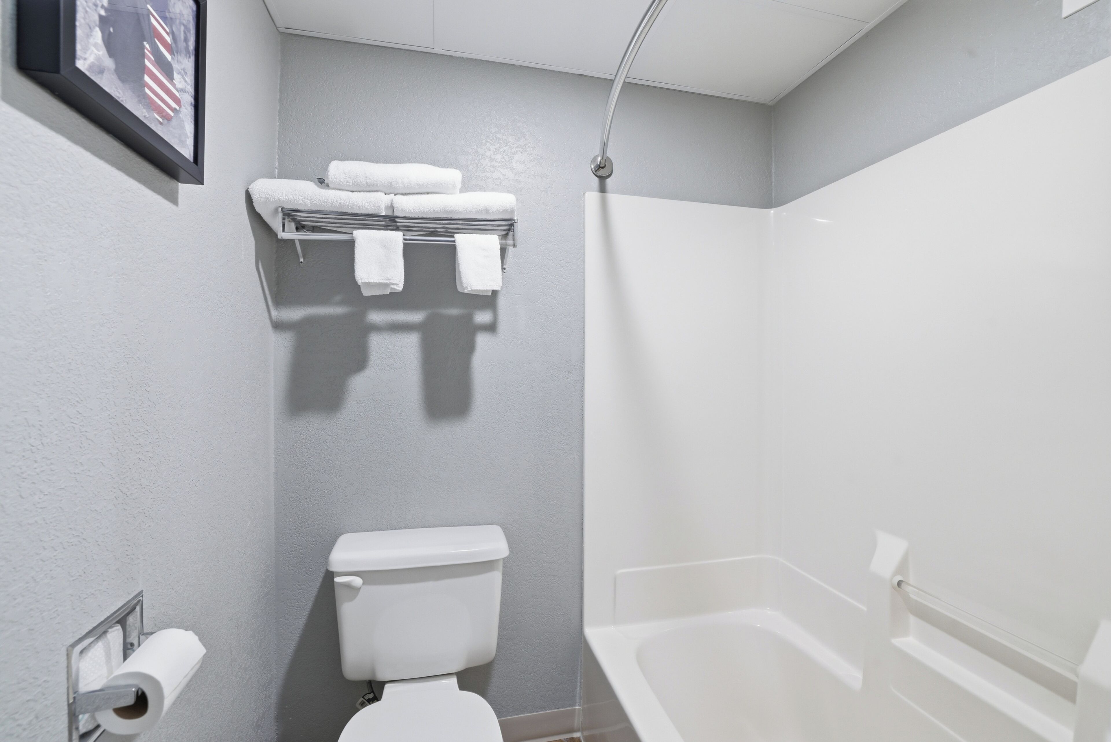 Casa de banho com sanita, um porta-toalhas com toalhas, área de duche e um quadro emoldurado na parede.
