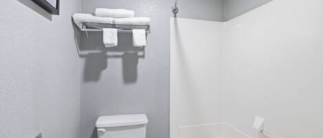 Casa de banho com sanita, um porta-toalhas com toalhas, área de duche e um quadro emoldurado na parede.