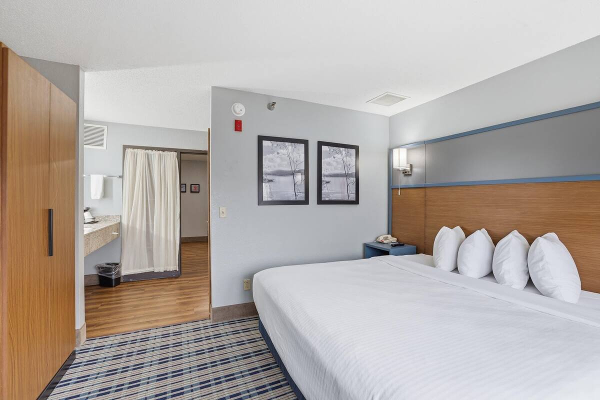 Une chambre d’hôtel avec un lit, une table de chevet, une salle de bain avec un rideau de douche et deux tableaux encadrés au mur.