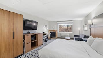 Quarto de hotel com cama, televisão, escrivaninha, cadeira, lareira e janela.