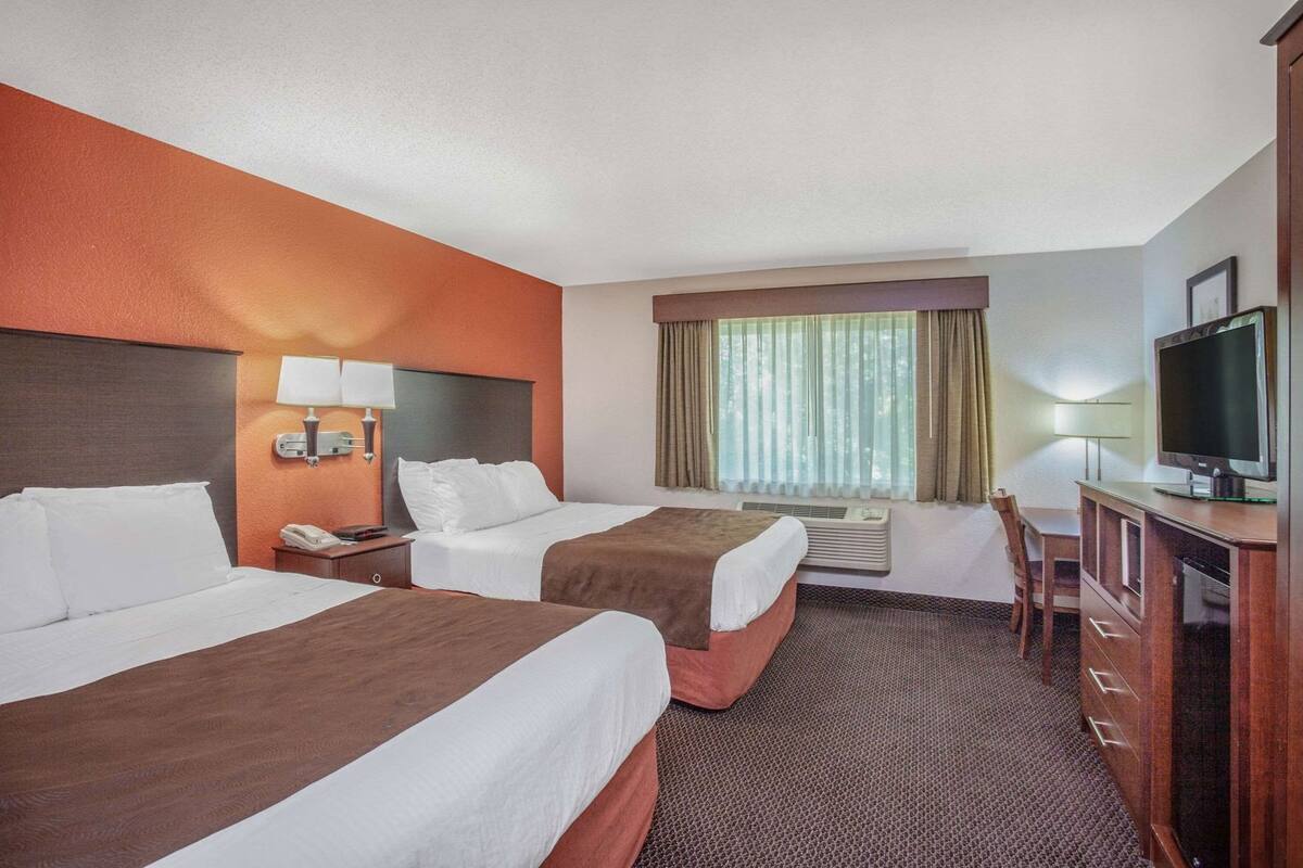 Une chambre d’hôtel avec deux lits, un bureau, une télévision et une fenêtre avec des rideaux.