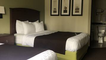 A hotel room with two beds, a nightstand, a wall-mounted lamp, and framed pictures.