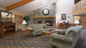 A spacious living room with a fireplace, a large clock, and a balcony. - Cobblestone Hotel & Suites – Wisconsin Rapids (Wisconsin Rapids)
