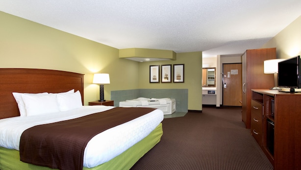 A hotel room with a large bed, a desk, a television, and a bathroom visible in the background. - Cobblestone Hotel & Suites – Wisconsin Rapids (Wisconsin Rapids)