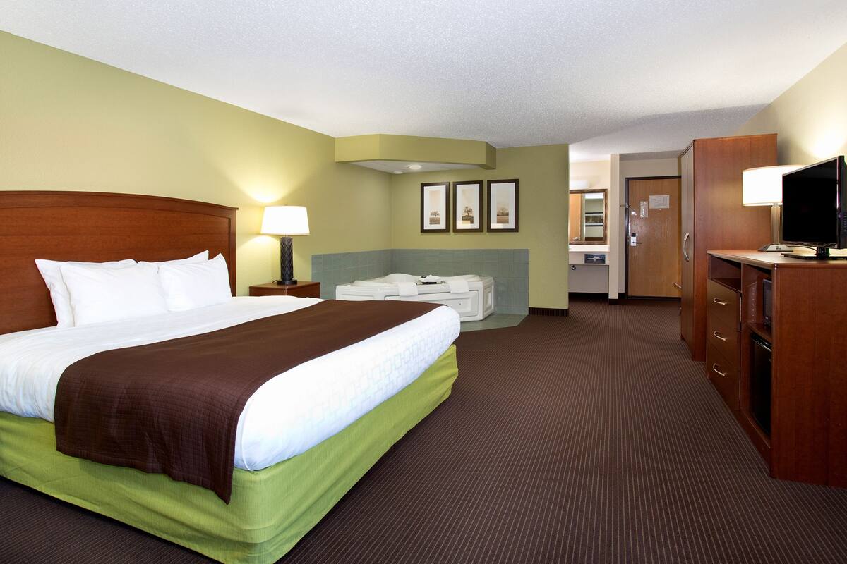 Une chambre d’hôtel avec un grand lit, un bureau, une télévision et une salle de bain visible au fond.