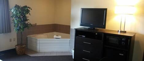 Une chambre d’hôtel avec une baignoire, un téléviseur posé sur un meuble, une plante et une lampe.