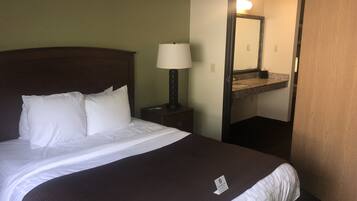 A hotel room with a bed, a nightstand with a lamp, a mirror, and a bathroom visible through an open door.