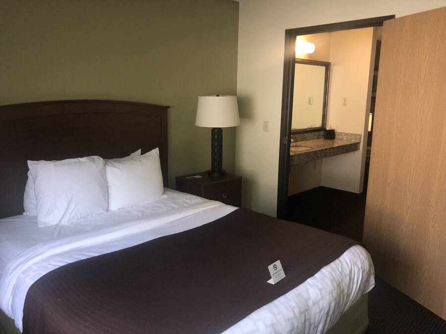 A hotel room with a bed, a nightstand with a lamp, a mirror, and a bathroom visible through an open door.
