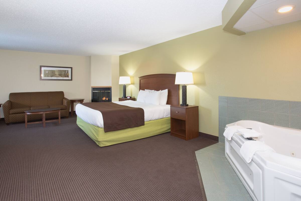 Une chambre d’hôtel comprenant un lit, un canapé, une table de chevet avec des lampes, une cheminée et une baignoire.
