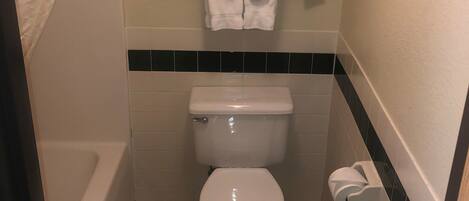 A small, clean bathroom with a toilet, a towel rack with folded towels, and a paper towel dispenser.