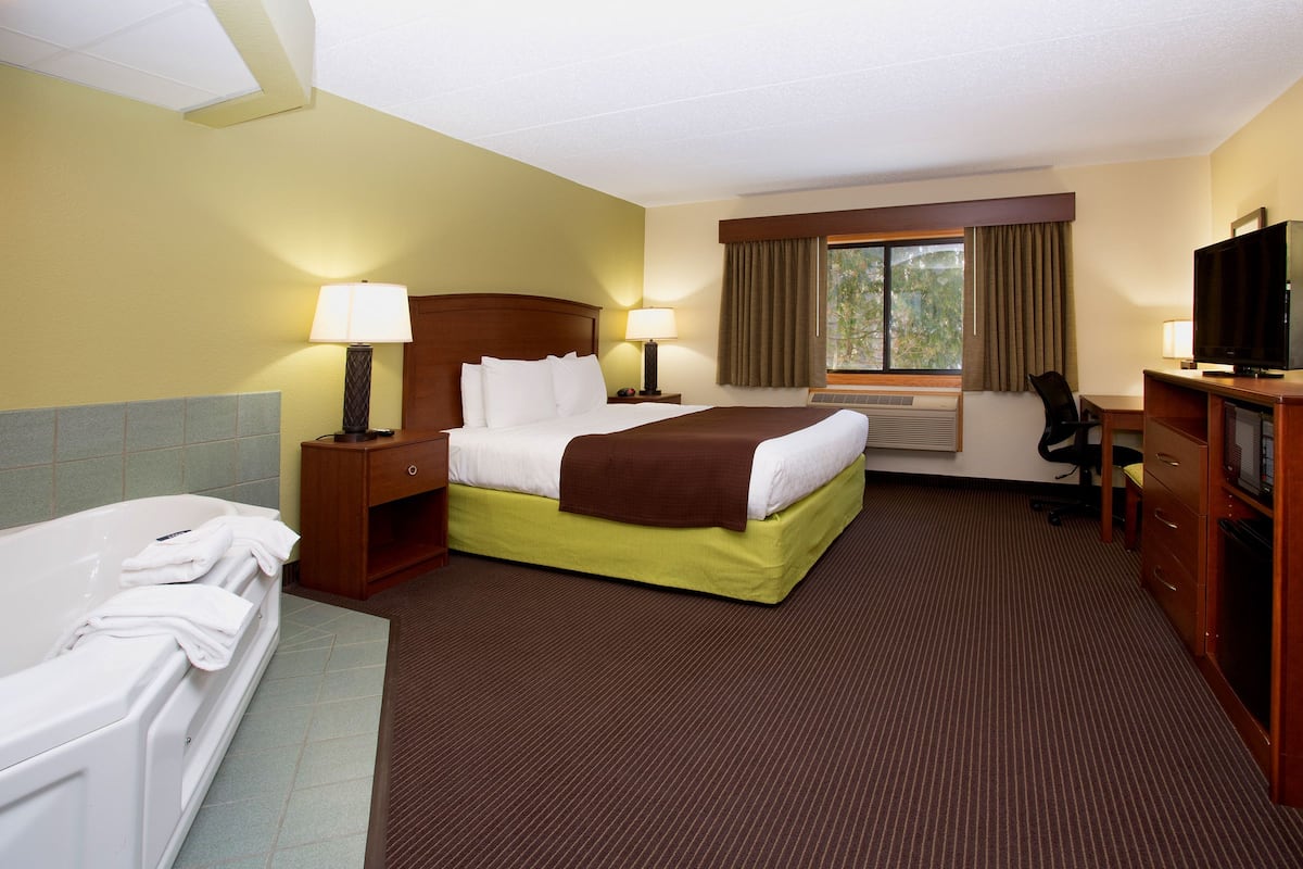 Une chambre d’hôtel avec un grand lit, un canapé-lit séparé, un bureau avec une chaise, une télévision et une fenêtre avec des rideaux.